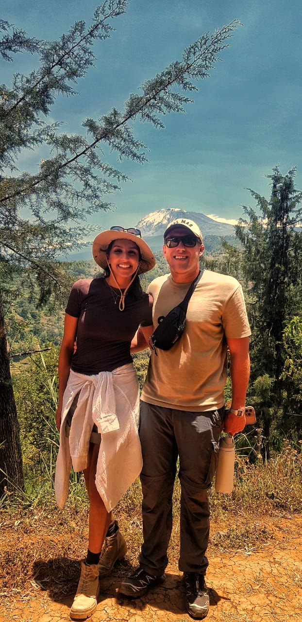 Two travelers on a hillside with Kilimanjaro behind them