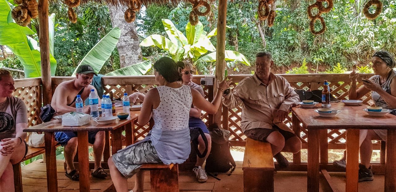 Guests sharing a meal at long tables under the thatched shelter